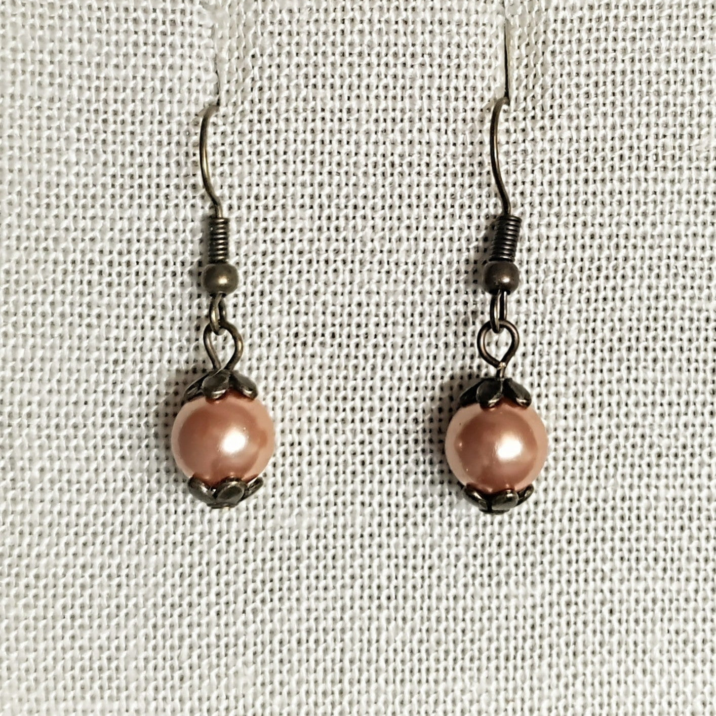 Pair of pink pearl earrings on a beige fabric background