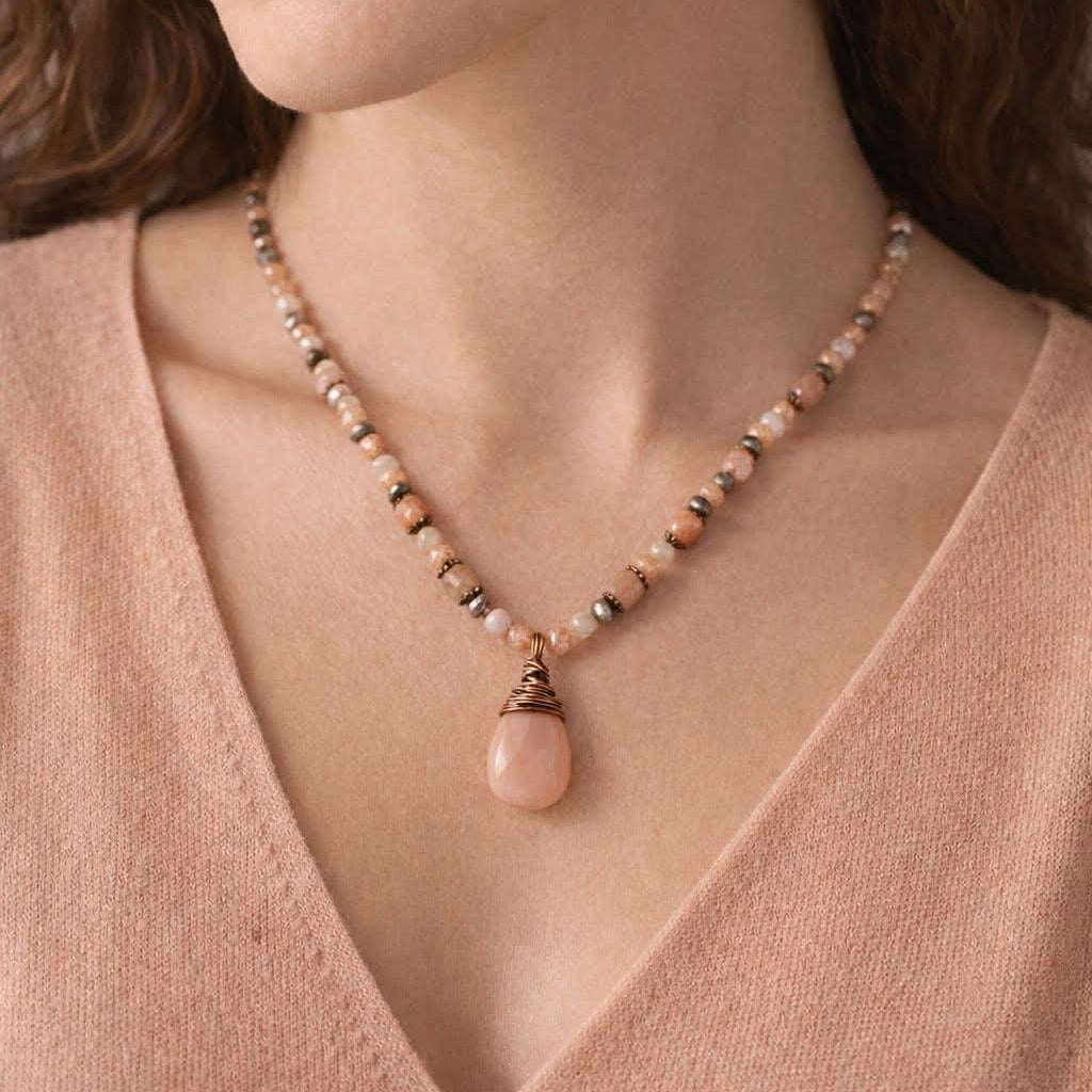 Necklace with a pink pendant worn by a person in a pink sweater.