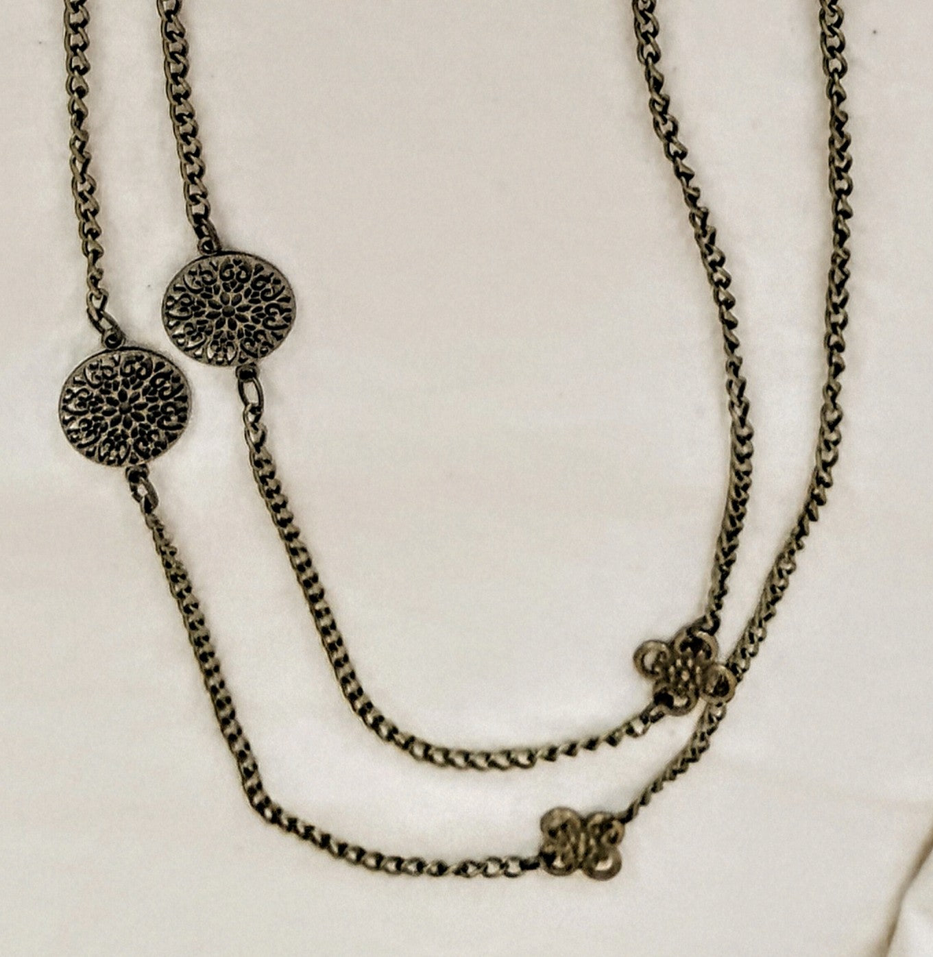 Two layered necklaces with floral and circular pendants on a light background
Chain detail