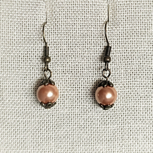 Pair of pink pearl earrings on a beige fabric background