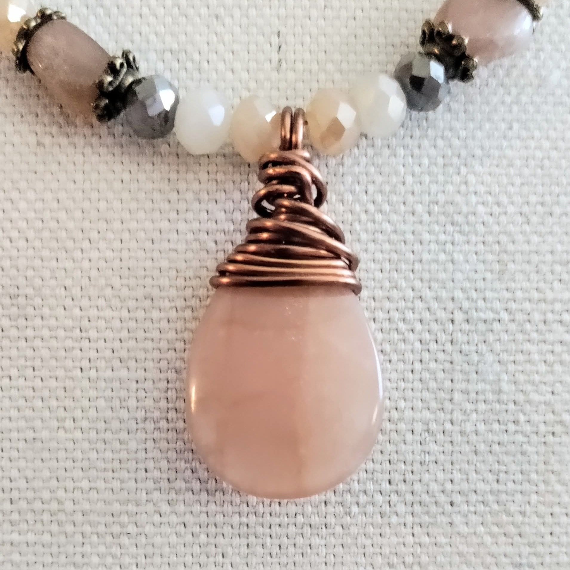 Necklace with pink teardrop pendant and beaded chain on a textured fabric background