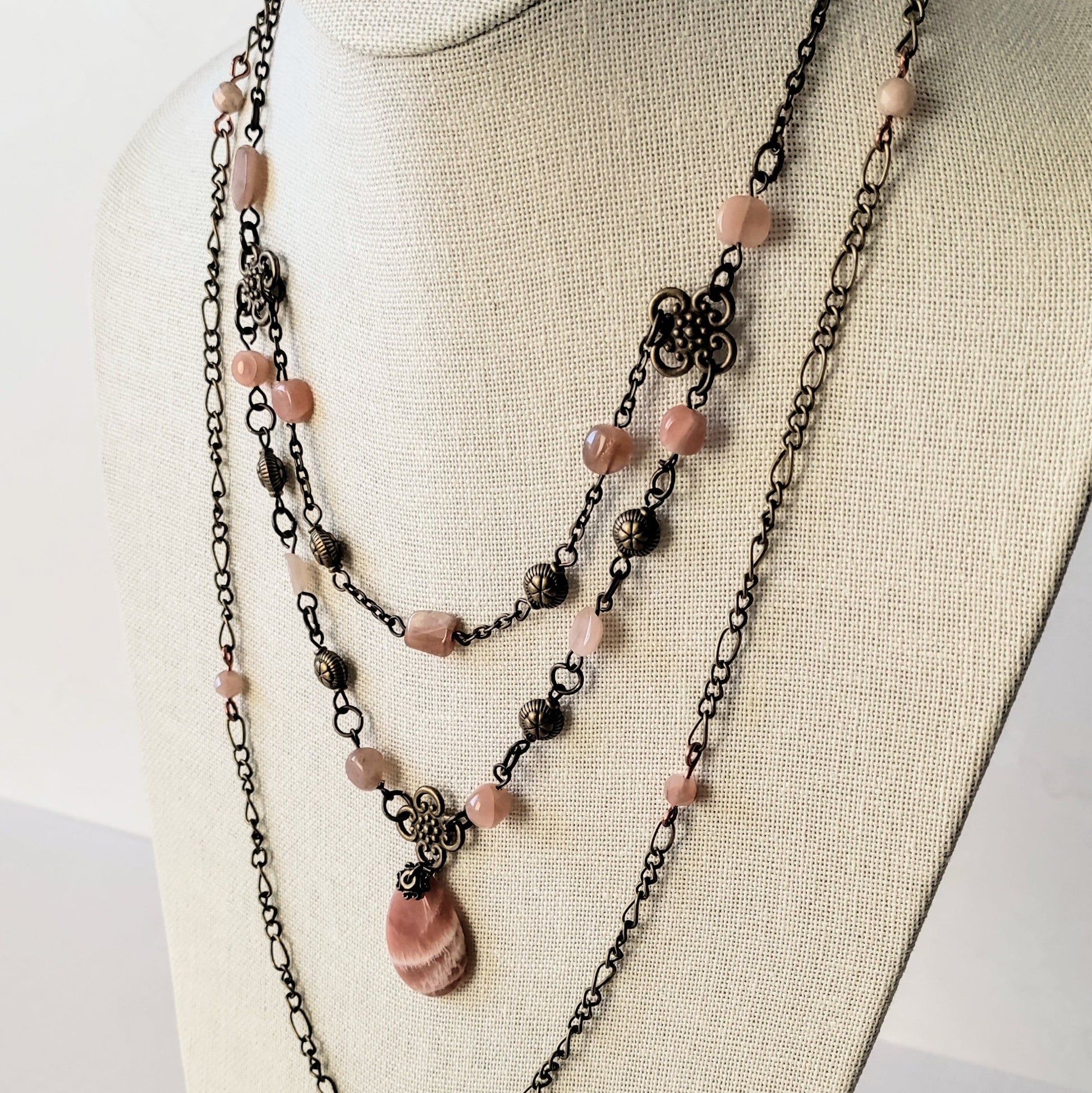 Layered necklace with peach moonstone beads and antiqued brass chain on a mannequin bust.