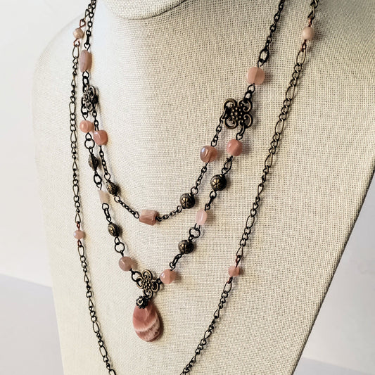 Layered necklace with peach moonstone beads and antiqued brass chain on a mannequin bust.