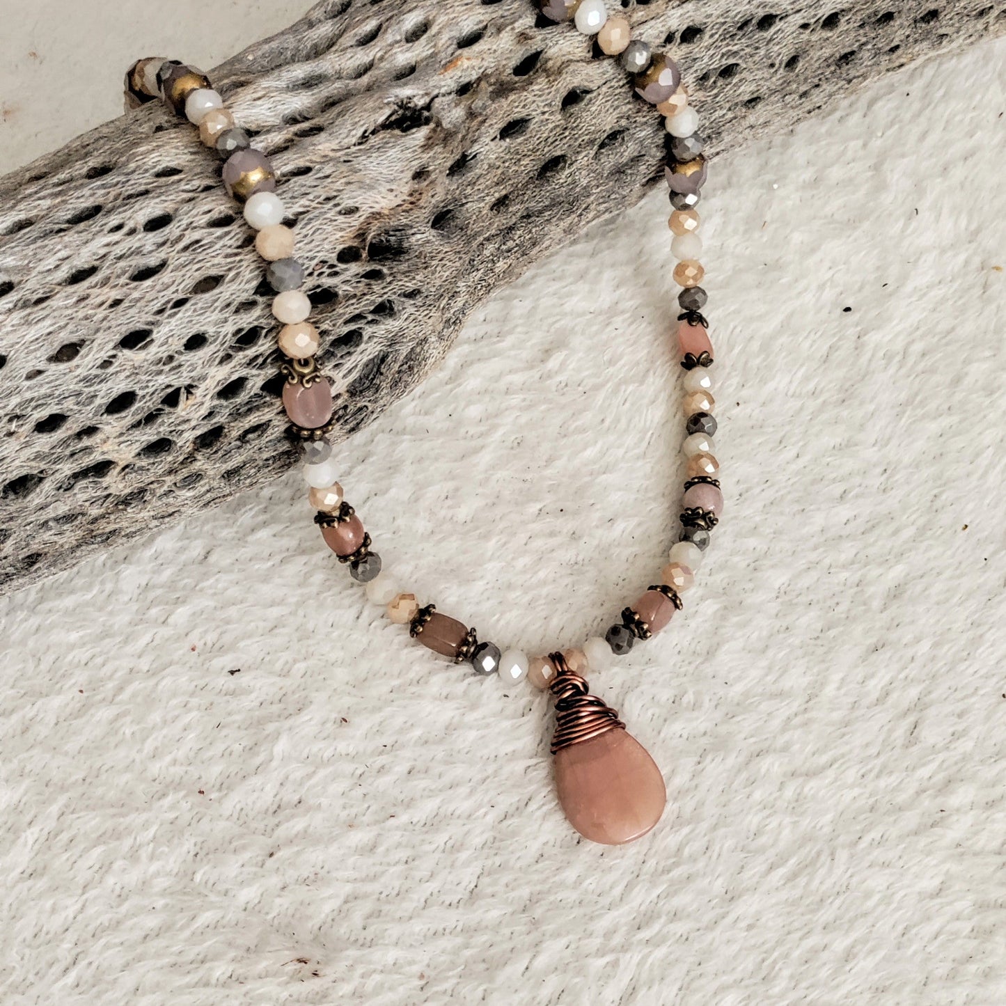 Necklace with beads and a pink stone pendant on a textured surface