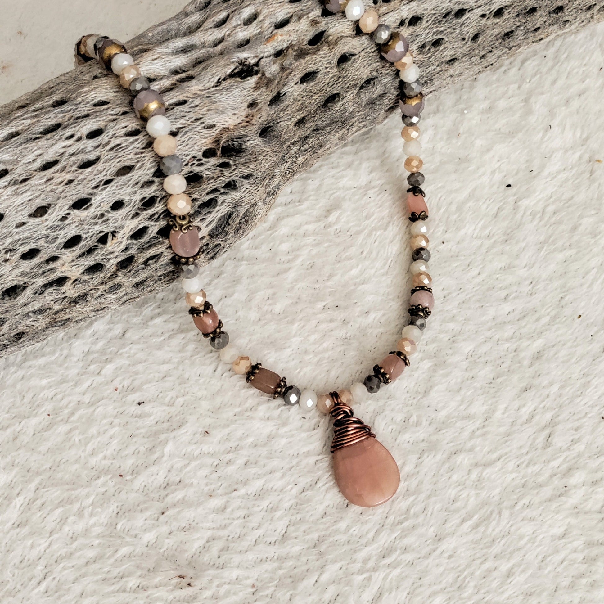 Necklace with beads and a pink stone pendant on a textured surface